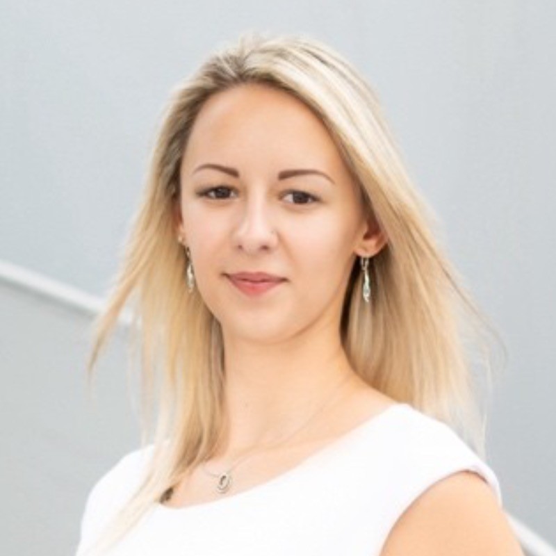 Věra Malurková. Usměvavá blond žena v bílém topu, jemné náušnice, portrét na světlém pozadí.